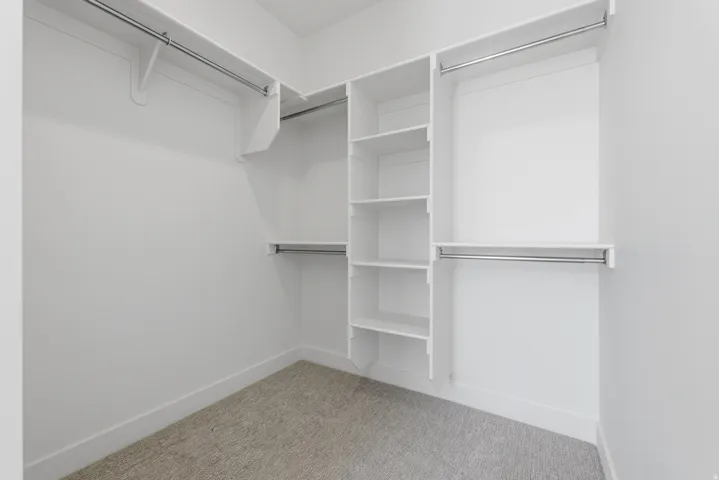 Walk-in closet with built-in shelving, multiple hanging rods, and neutral-toned carpeting