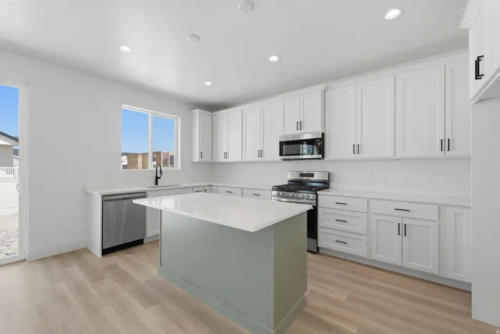 Modern kitchen featuring white shaker cabinetry, stainless steel appliances, a center island with a light-toned countertop, wood-finish flooring, and a sliding glass door