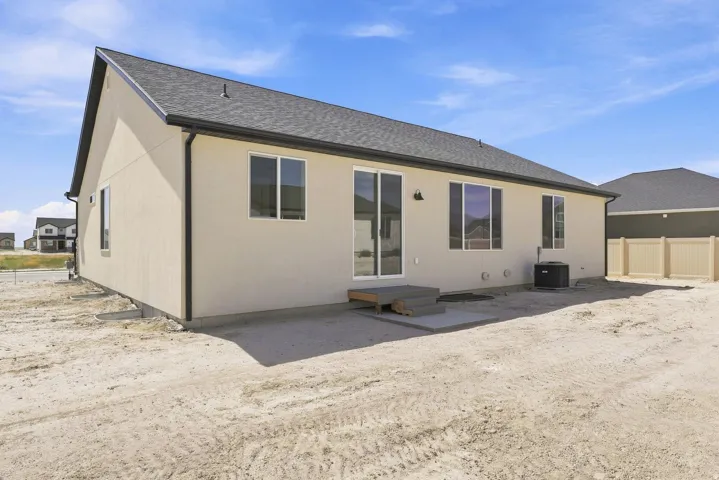 Contemporary stucco exterior with a dark shingled roof, featuring a sliding glass door, multiple windows, and a rear concrete patio
