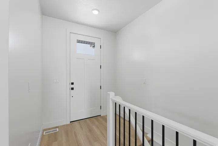 Entryway featuring a white paneled door with transom window, recessed lighting, wood-finish flooring, and a staircase with white railing and black balusters