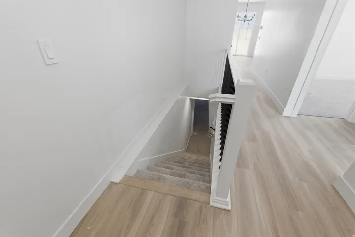 Light wood-finish flooring, white painted walls, white trim, and a staircase with carpeted treads and a white banister