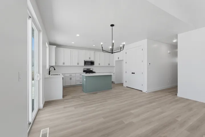 Open-concept living area featuring wood-finish flooring, a contemporary chandelier, white cabinetry, a contrasting island, and a sliding glass door