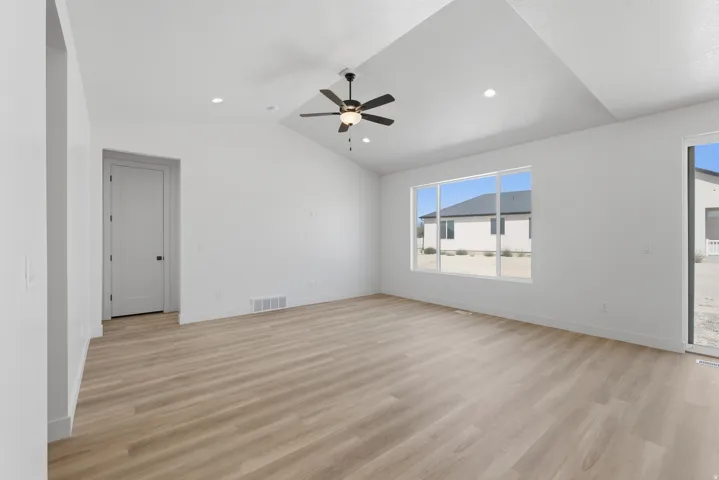 Vaulted ceiling with a ceiling fan, recessed lighting, wood-finish flooring, a large multi-pane window, and a glass sliding door