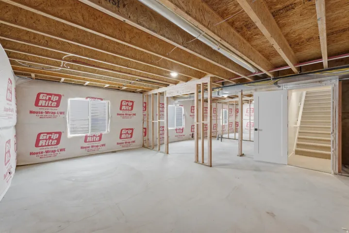 Unfinished basement featuring exposed wood joists, framed wall sections, and multiple windows