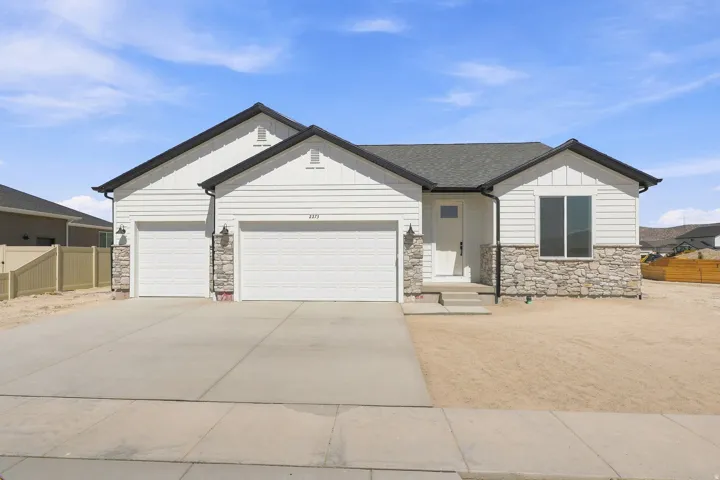 Single-story exterior with white siding, stone veneer accents, dark shingle roof, two-car garage, and concrete driveway