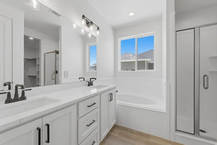 Dual vanity with matte black fixtures, built-in soaking tub, glass-enclosed shower, wood-finish flooring, and recessed lighting