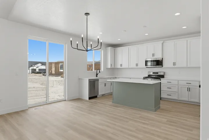 Contemporary kitchen with white cabinetry, light wood-finish flooring, a central island, stainless steel appliances, and a modern chandelier