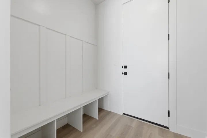 Built-in bench with storage, vertical paneling, light wood-finish flooring, and a modern door with matte black hardware