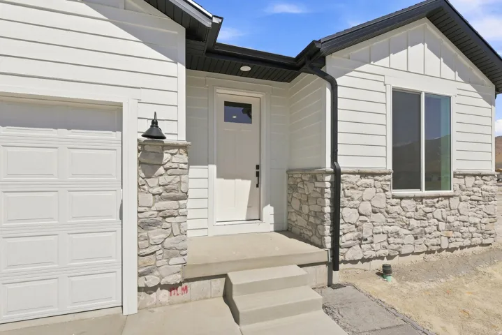 White siding exterior with stone accents, a concrete front entry, and a paneled garage door