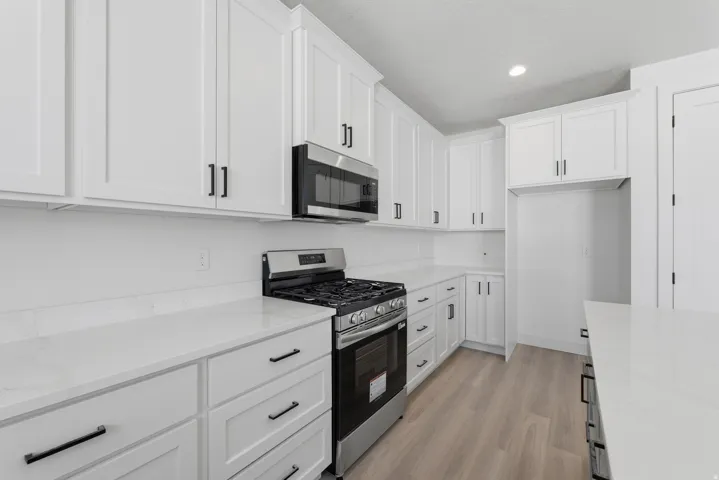 White shaker-style cabinetry with matte black hardware, stainless steel range and microwave, light-toned countertops, and wood-finish flooring