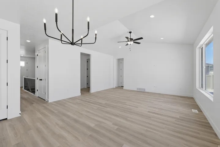 Spacious room featuring wood-finish flooring, vaulted ceilings, a contemporary chandelier, recessed lighting, and a ceiling fan
