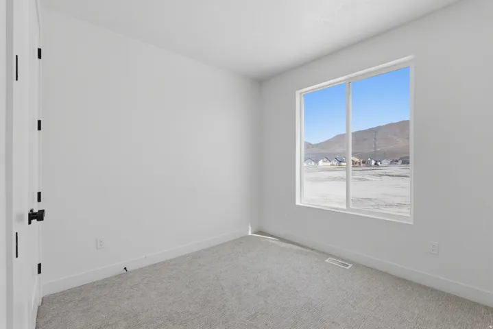 Light gray carpeting, a white door with black hardware, white walls, and a large window with a mountain backdrop