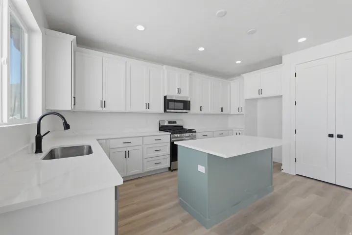 Modern kitchen featuring white cabinetry, light-toned wood-finish flooring, a central island with a contrasting base, stainless steel appliances, and recessed lighting