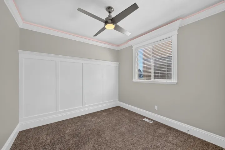 Board and batten wall treatment, crown molding with accent lighting, window with blinds, ceiling fan with integrated lighting, and carpeted flooring