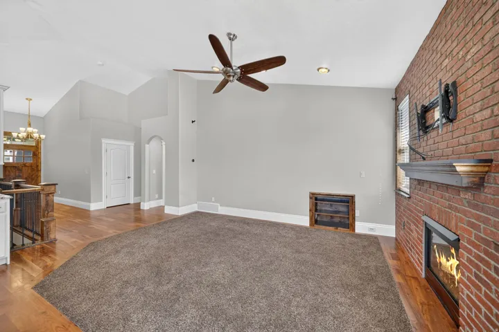 Vaulted ceilings, wood-finish flooring, exposed brick wall, built-in fireplace, and a ceiling fan