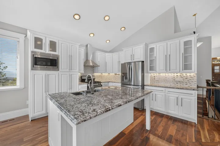 Open-concept kitchen with white cabinetry, stainless steel appliances, granite countertops, and wood-finish flooring