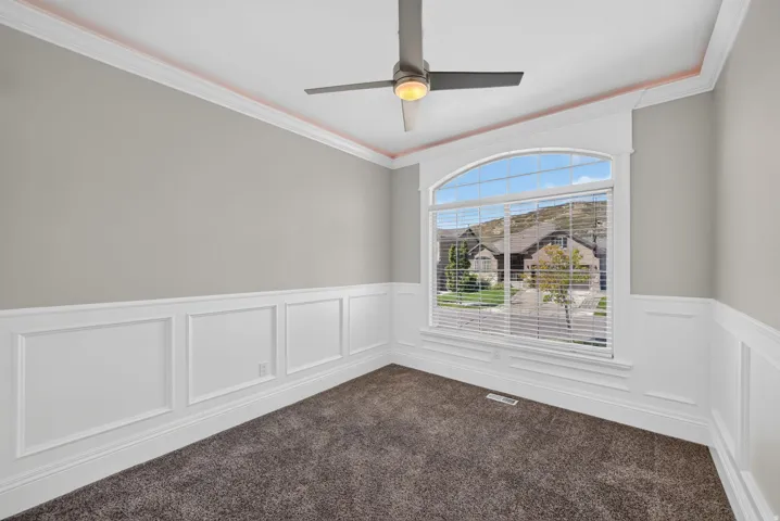 Arched window, crown molding, wainscoting, ceiling fan with integrated lighting, and plush carpeting