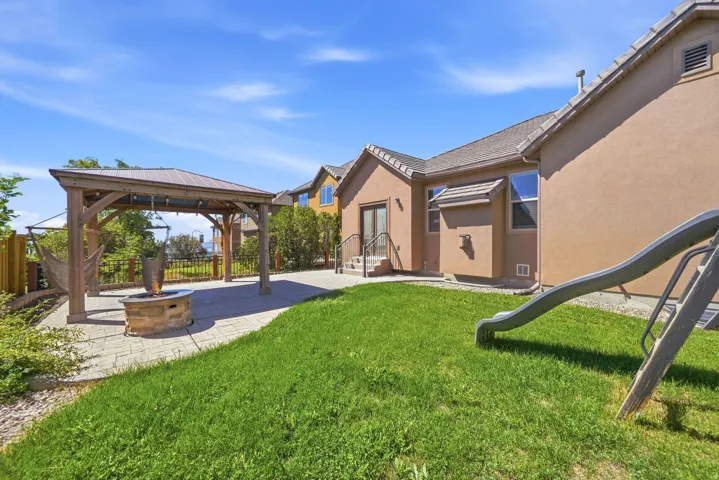 Expansive backyard featuring a stone-paver patio, a wooden pergola, and a built-in stone fire pit