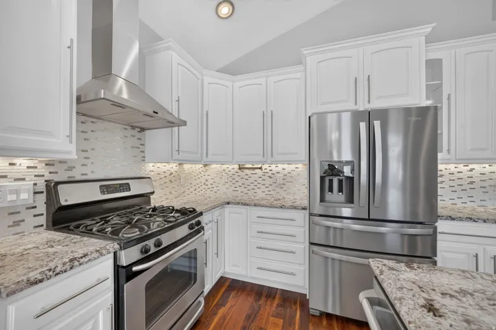 White cabinetry, stainless steel appliances, granite countertops, tile backsplash, and wood-finish flooring