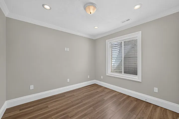 Wood-finish flooring, recessed lighting, crown molding, a window with blinds, and neutral wall tones