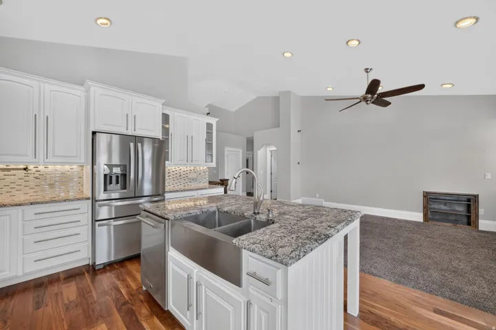 Kitchen island with a double basin stainless steel farmhouse sink, white cabinetry, integrated stainless steel appliances, and wood-finish flooring