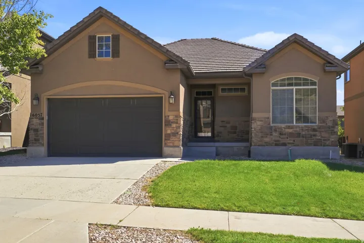 Stucco exterior with stone accents, arched entryway, multi-pane windows, front lawn, and attached garage