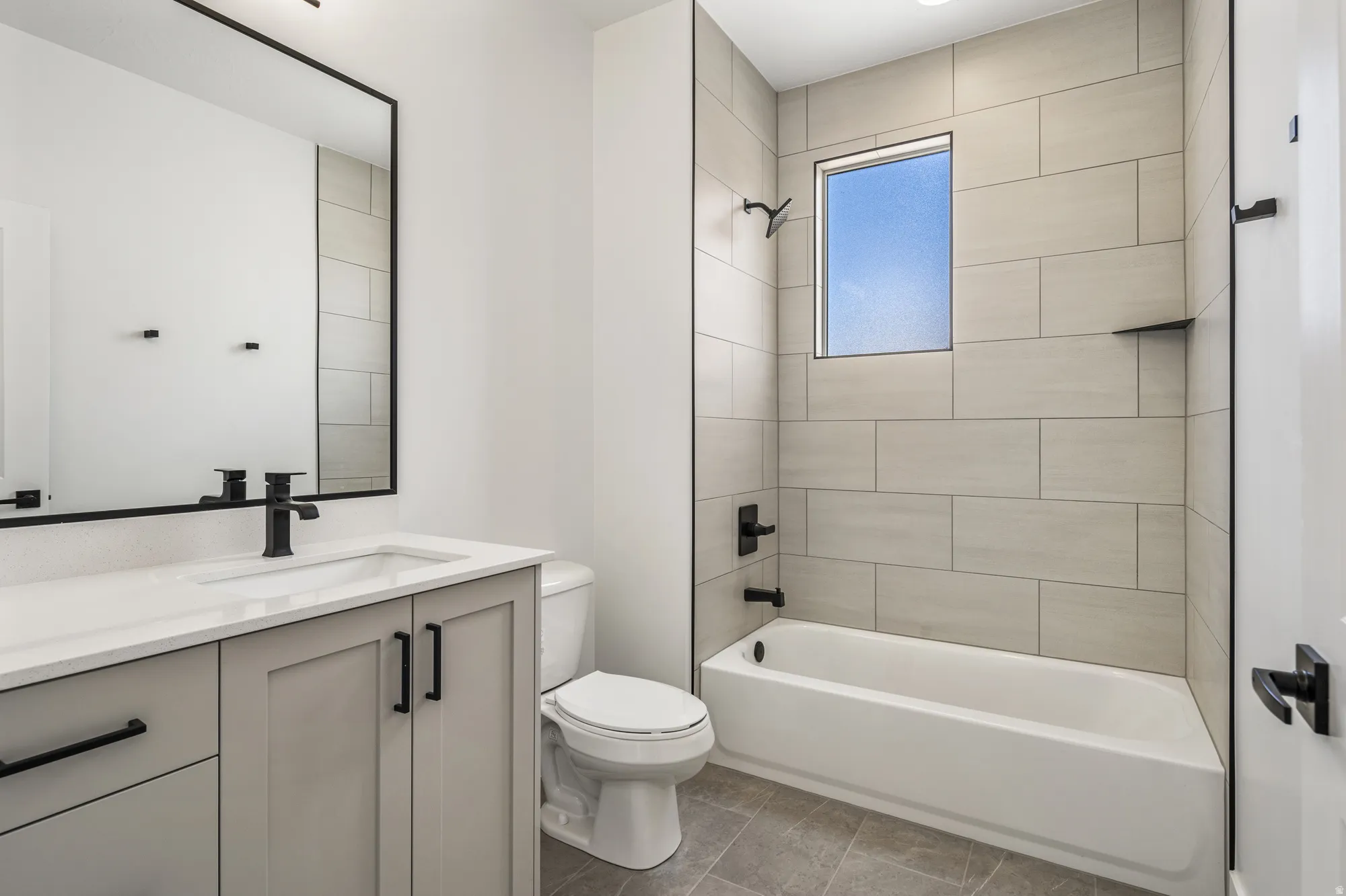 Modern vanity with integrated sink and matte black faucet, framed mirror, and a tiled shower-bathtub combination with matte black fixtures
