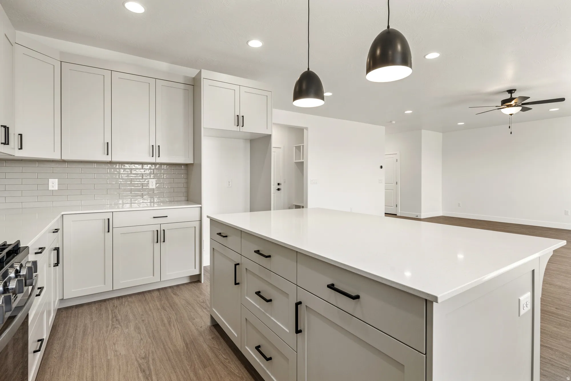Kitchen featuring light-toned cabinetry, a spacious island with a solid surface countertop, subway tile backsplash, and wood-finish flooring