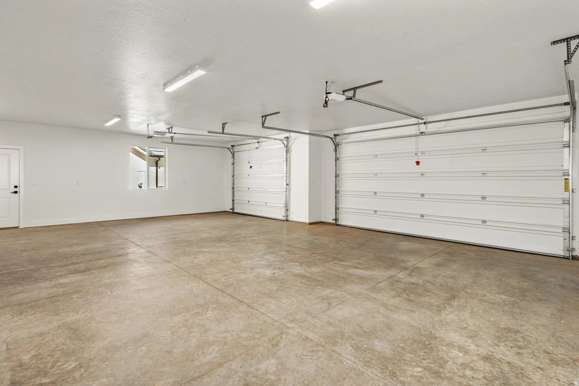 Spacious three-car garage featuring concrete flooring, automatic garage doors, and overhead strip lighting