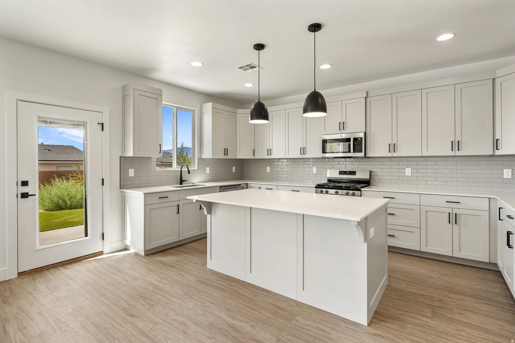 Modern kitchen featuring wood-finish flooring, light gray cabinetry with black hardware, a center island with a white countertop, and stainless steel appliances