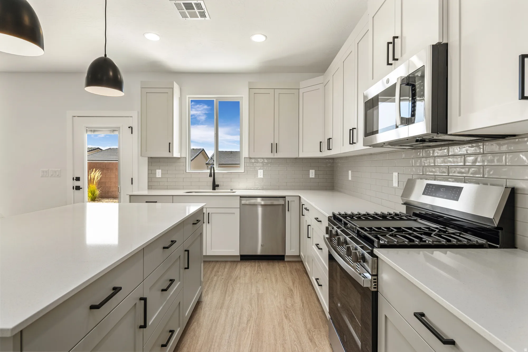 Spacious kitchen with a large island, stainless steel appliances, extensive cabinetry, light-toned countertops, and a subway tile backsplash