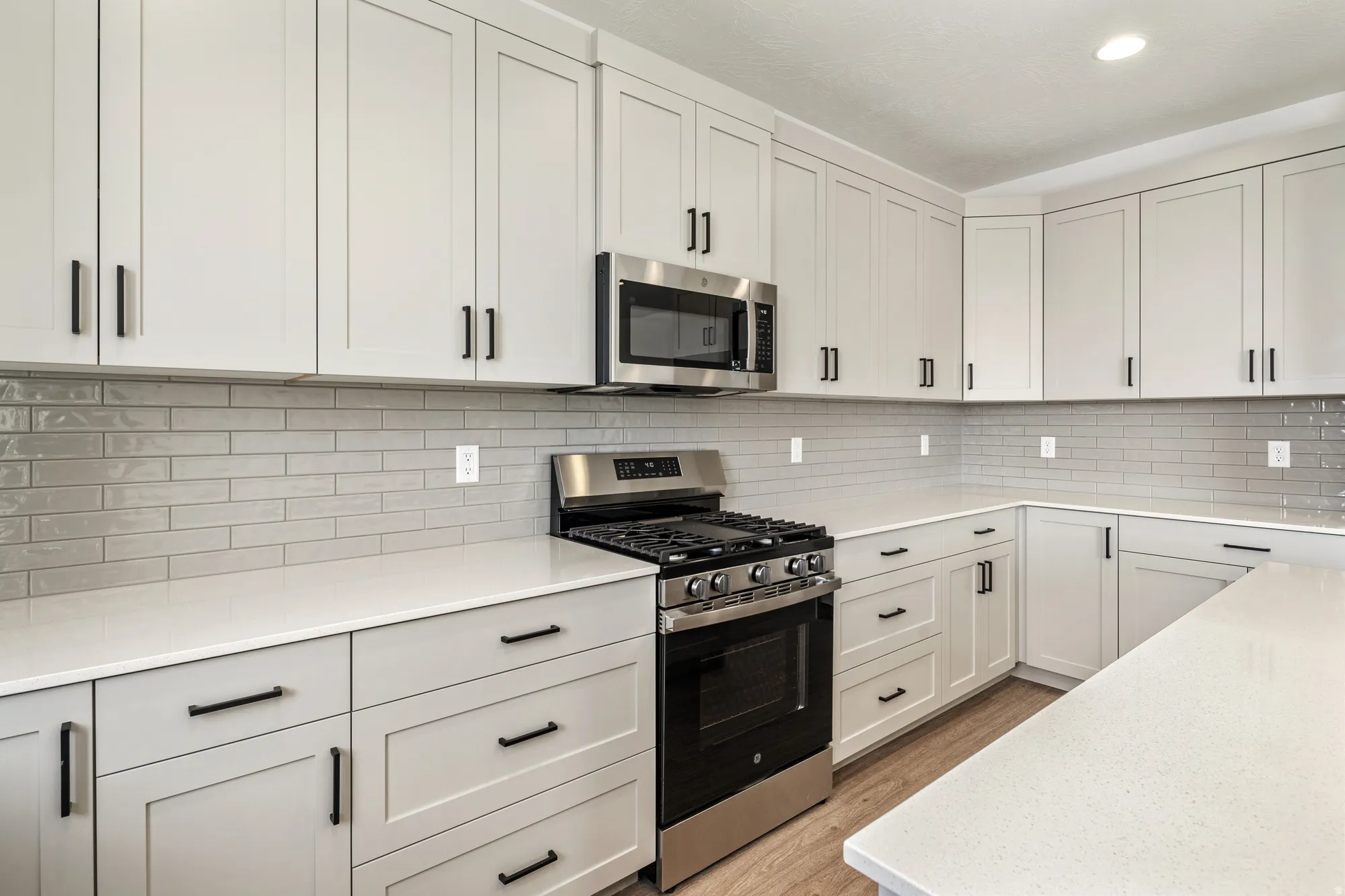 White shaker cabinetry with matte black hardware, subway tile backsplash, white countertops, stainless steel range, and stainless steel microwave
