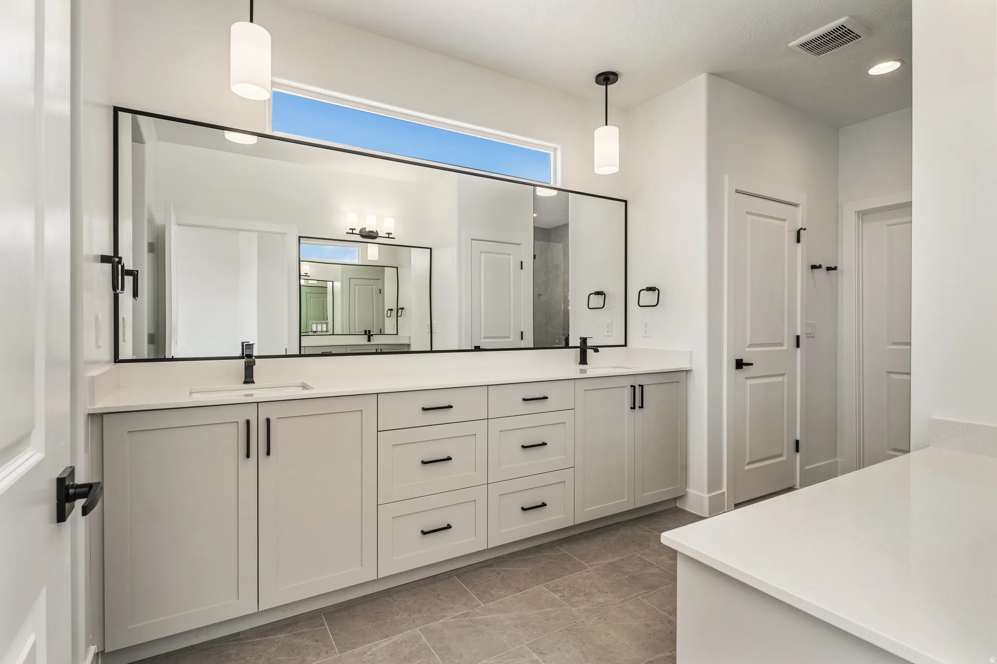 Dual vanity with white shaker cabinetry, matte black hardware, and an expansive integrated mirror