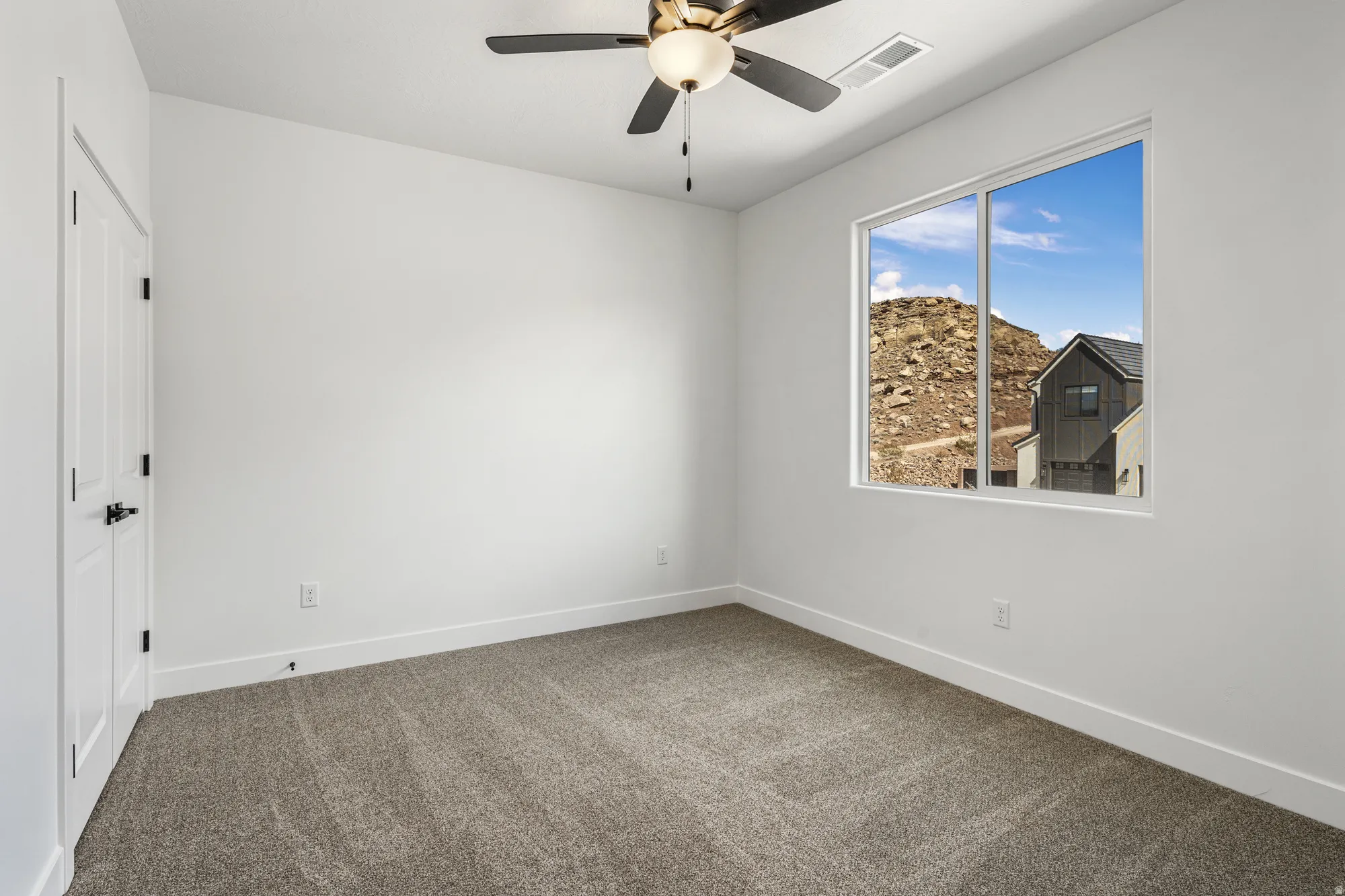 Bright room with neutral wall color, plush carpet flooring, a modern ceiling fan, and a large window