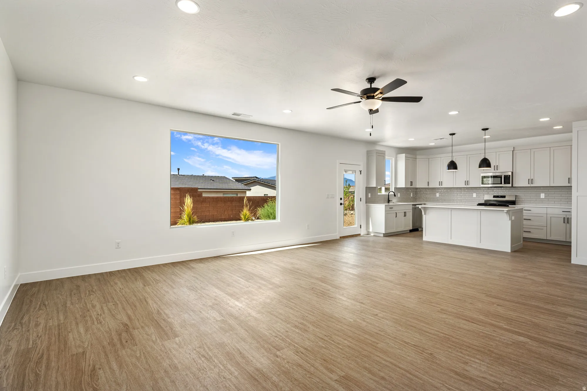 Spacious open-concept interior featuring wood-finish flooring, recessed lighting, a ceiling fan, a kitchen island, and white shaker cabinetry