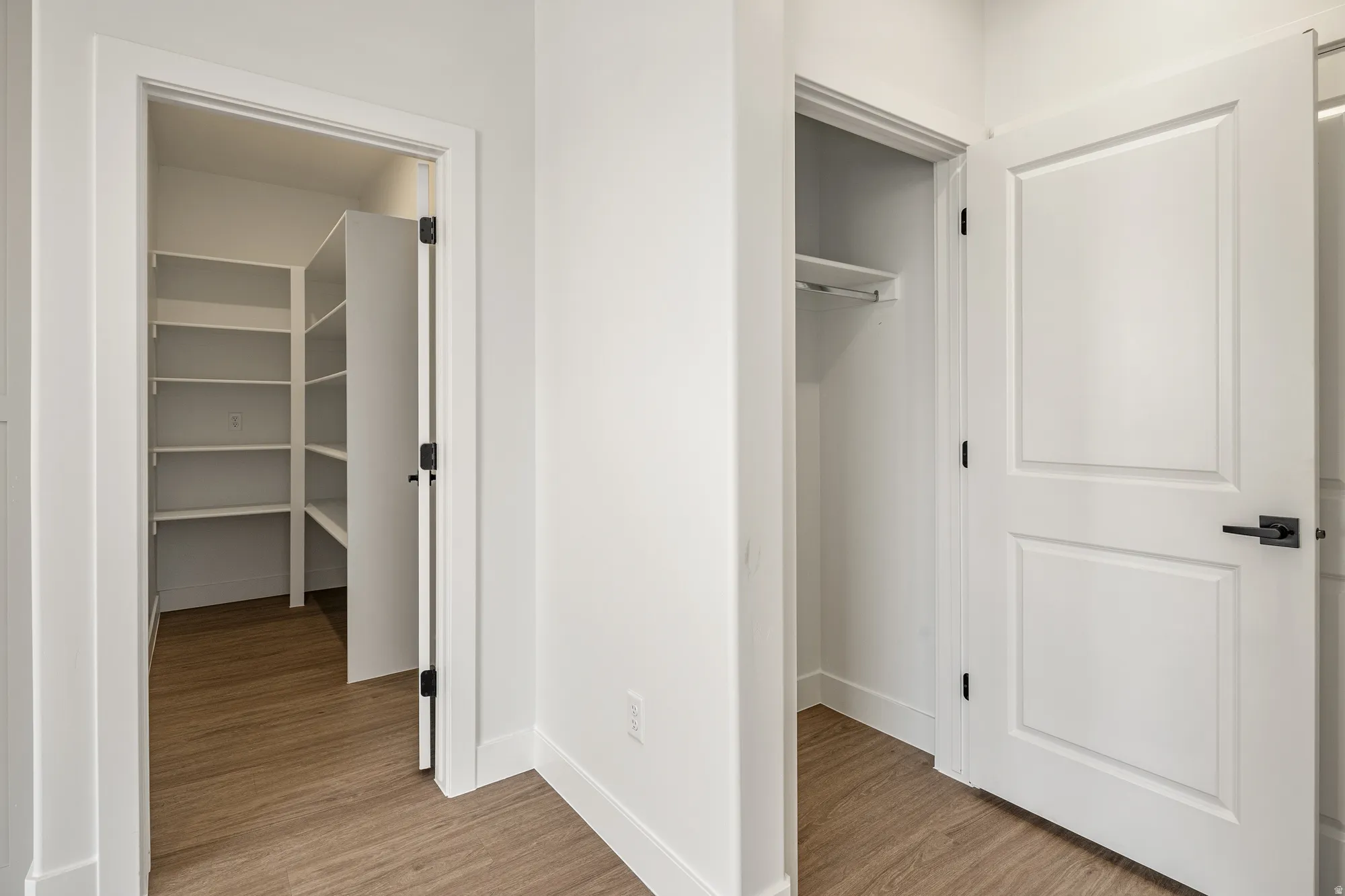 Wood-finish flooring, white walls, white trim, white paneled doors, and matte black hardware