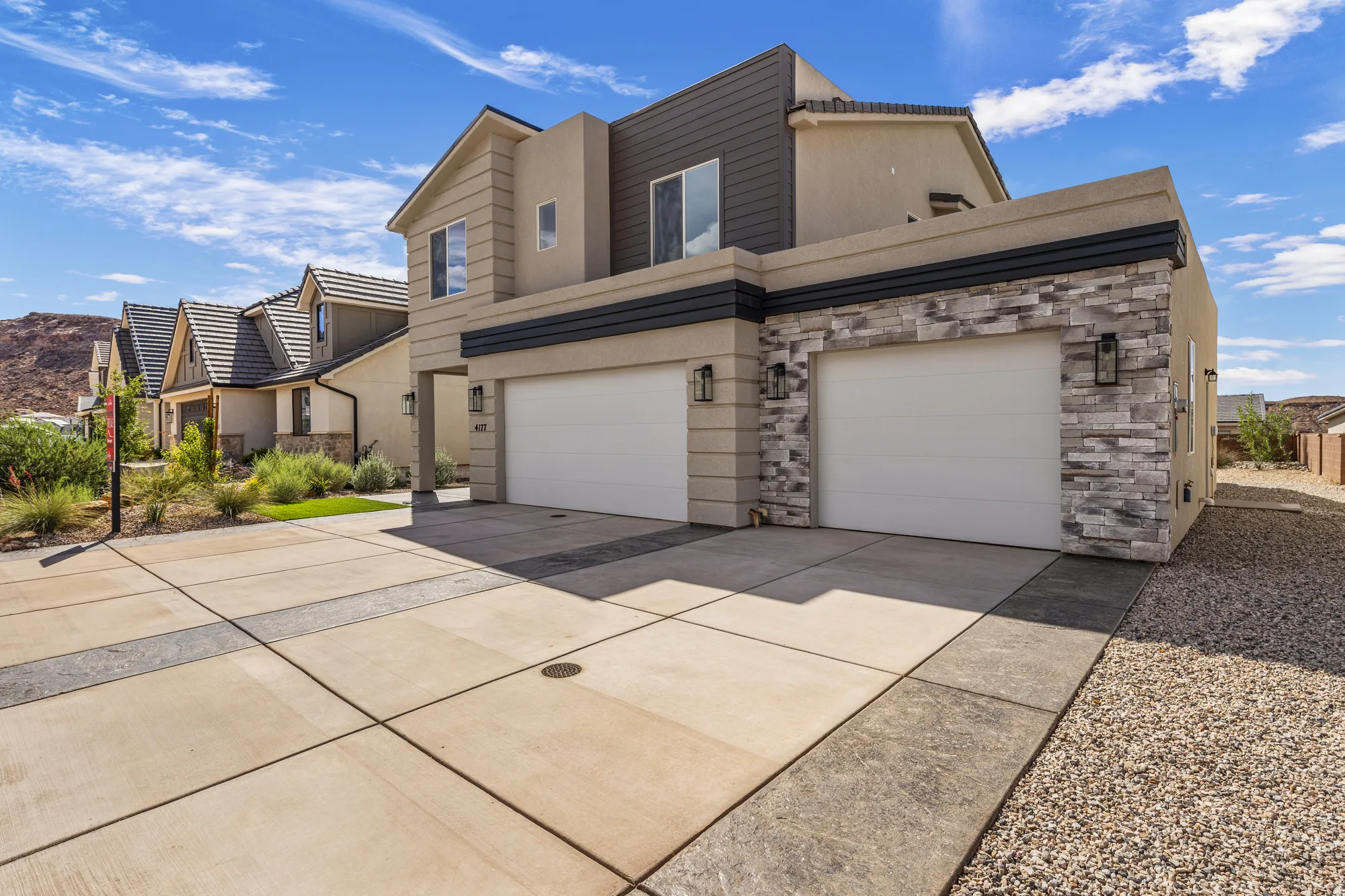Contemporary exterior with stacked stone accents, two garage doors, stucco siding, and a concrete driveway with decorative inlays