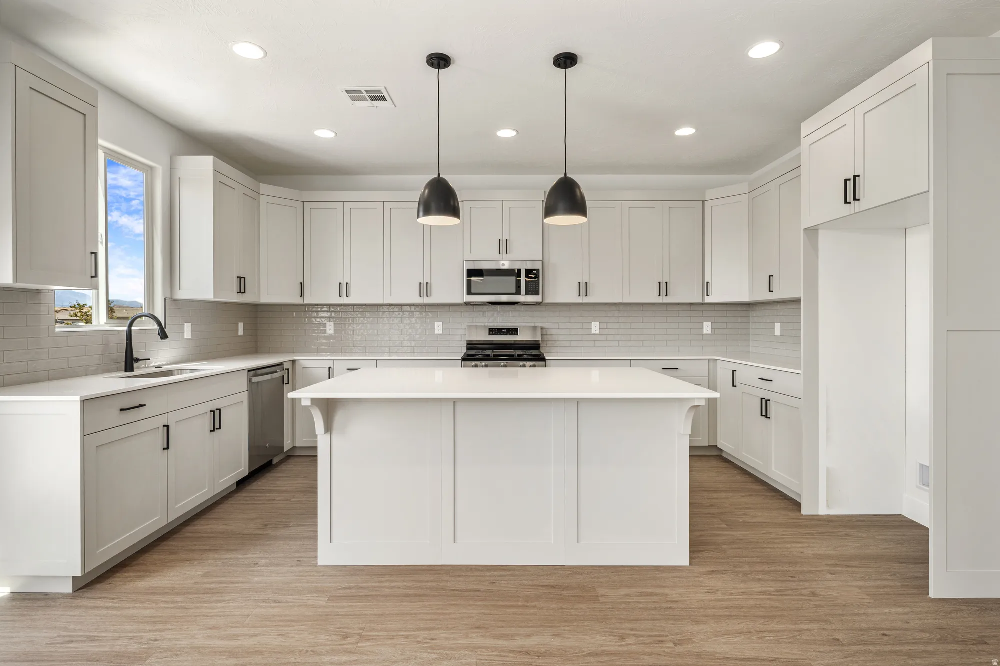 Modern kitchen featuring an expansive center island, white shaker-style cabinetry, subway tile backsplash, stainless steel appliances, and wood-finish flooring