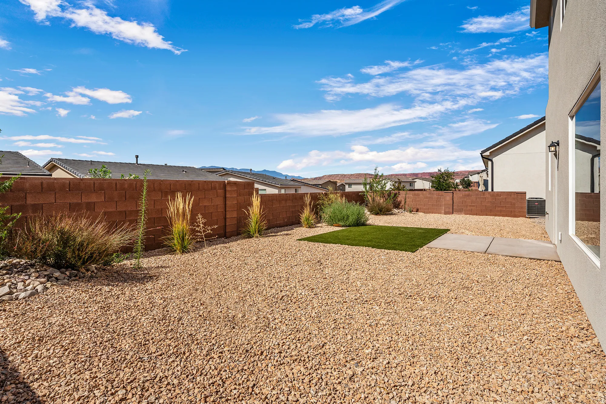 Expansive outdoor space featuring gravel landscaping, a privacy block wall, a small artificial turf area, and integrated shrubbery