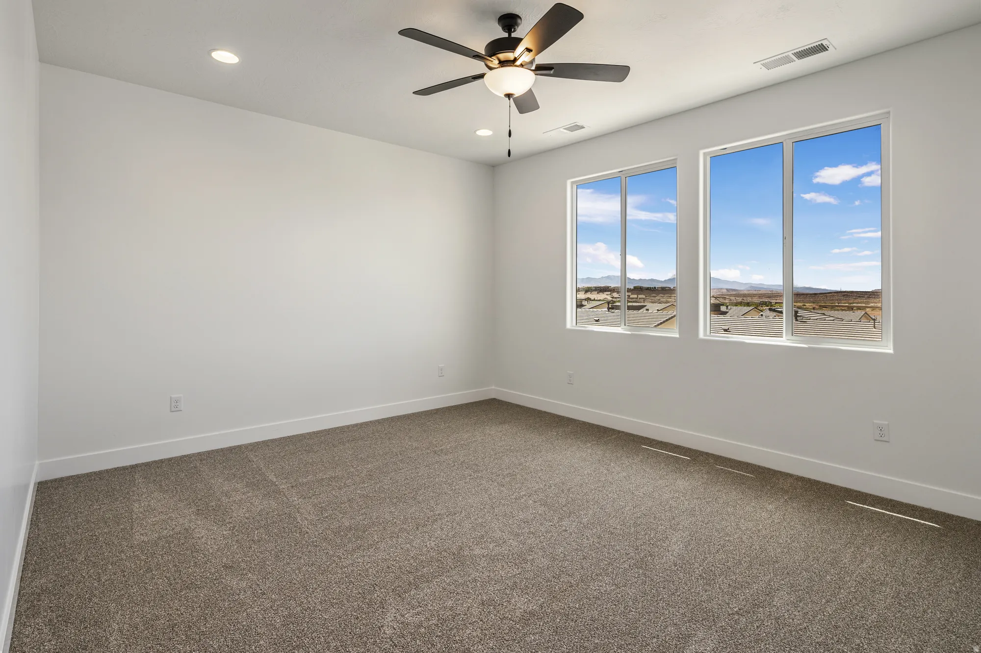 Dual large windows, recessed ceiling lighting, a ceiling fan with integrated lighting, and neutral carpeting