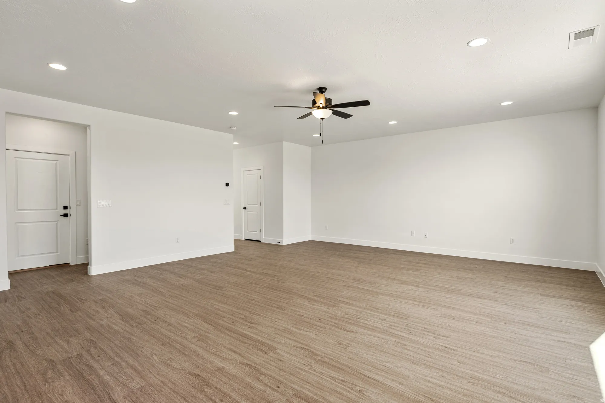 Spacious room featuring wood-finish flooring, recessed lighting, and a ceiling fan