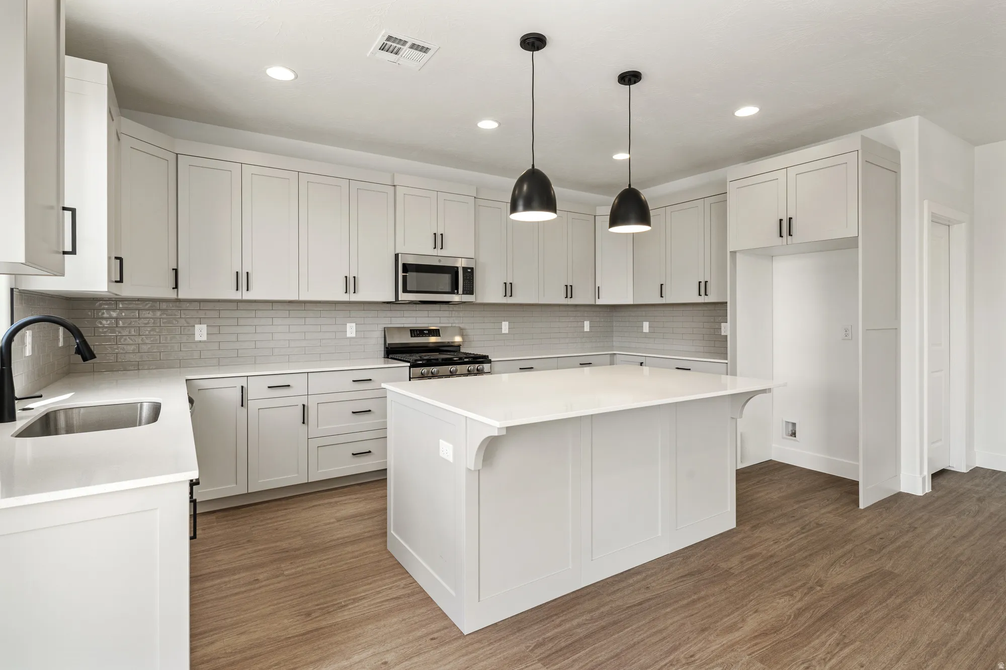 Kitchen featuring white cabinetry with black hardware, white countertops, stainless steel appliances, and wood-finish flooring