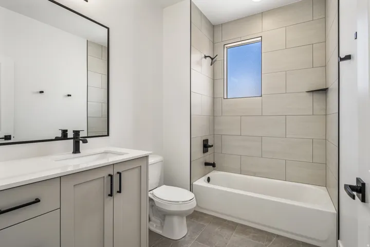 Modern vanity with integrated sink and matte black faucet, framed mirror, and a tiled shower-bathtub combination with matte black fixtures