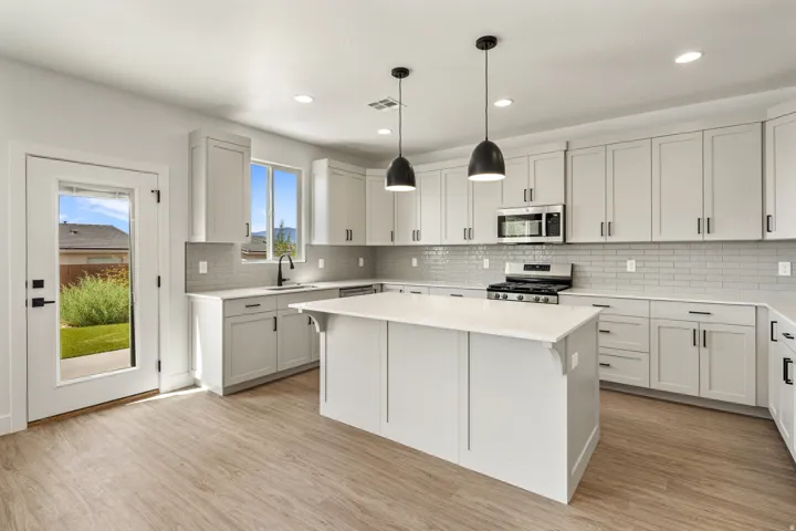 Modern kitchen featuring wood-finish flooring, light gray cabinetry with black hardware, a center island with a white countertop, and stainless steel appliances