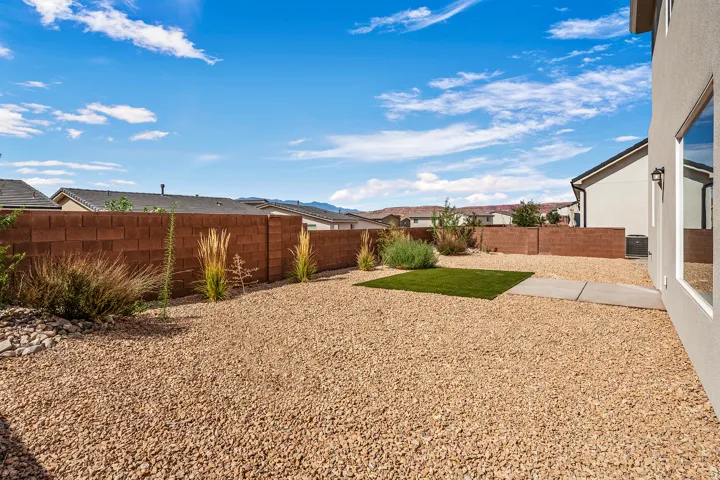 Expansive outdoor space featuring gravel landscaping, a privacy block wall, a small artificial turf area, and integrated shrubbery