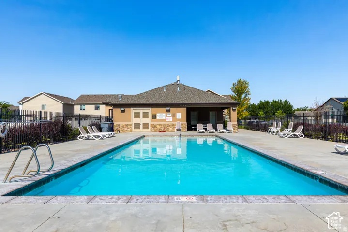 Outdoor swimming pool with concrete decking, surrounding black metal fencing, and an adjacent building featuring stone veneer accents