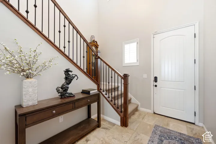 Arched entry door, high ceilings, wood-finish console table, wrought iron and wood staircase, and tiled flooring
