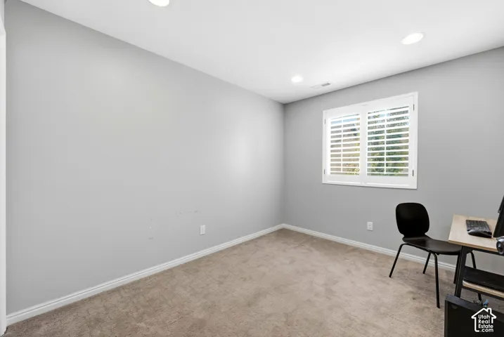 Recessed lighting illuminates this room featuring wall-to-wall carpeting and a window with white louvered shutters