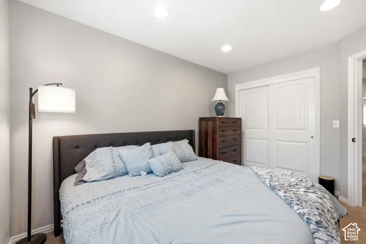 Neutral wall color, recessed ceiling lighting, upholstered headboard, sliding double-door closet, and wood-finish dresser
