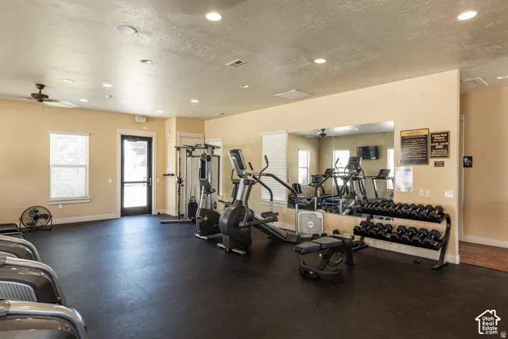 Fitness area with rubber flooring, integrated ceiling lights, a ceiling fan, and a mirrored wall
